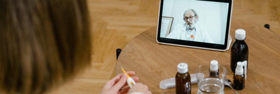 A doctor provides an online consultation via video call on a tablet, seen on a wooden table.