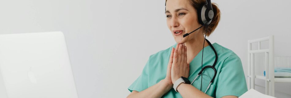 Female nurse using telemedicine for a virtual consultation on a laptop, wearing headphones and stethoscope.